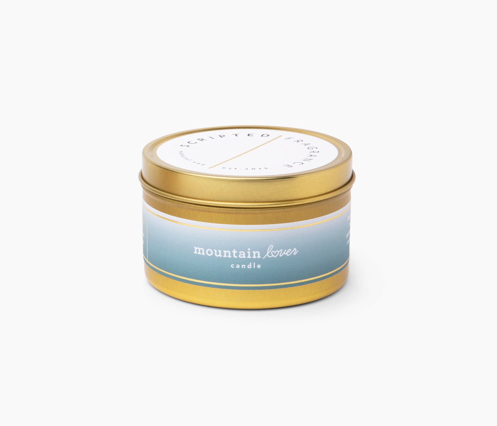 Fun soy candle labeled “Mountain Lover” in gold travel tin
